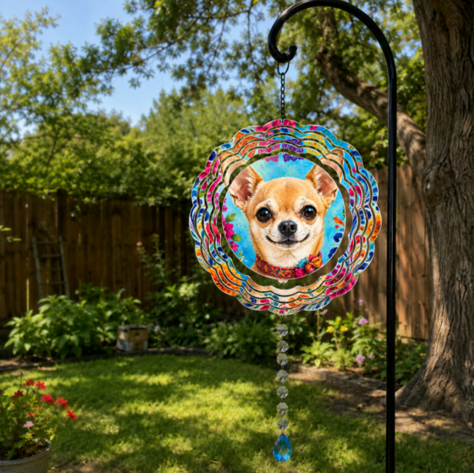 A circular metal garden suncatcher with a colorful floral border and a portrait of a chihuahua dog in the center, hanging from a black metal garden stake in a sunny backyard garden.