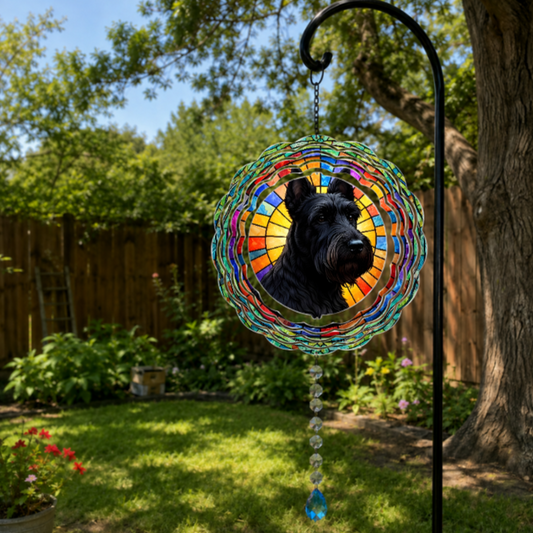 A circular stained-glass-style garden ornament featuring a black dog portrait, hanging from a black metal garden stake in a sunny backyard with grass, trees, and a wooden fence.